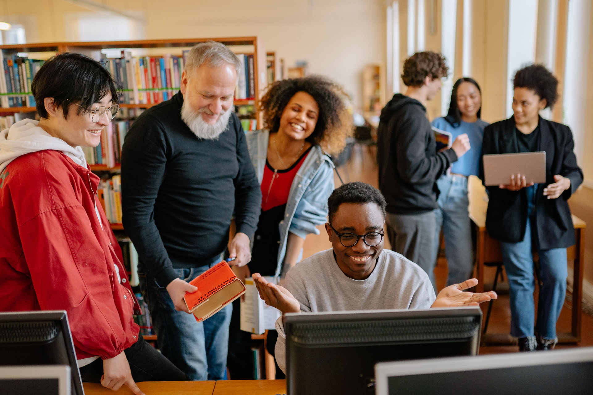 Students and mentor laughing together around a computer in a library